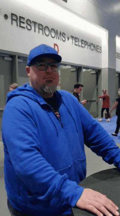 A Man In A Blue Jacket Stands In Front Of A Sign That Says Restrooms And Telephones GIF