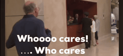 A Man In A Blue Jacket Stands In Front Of A Sign That Says Who Cares Who Cares GIF