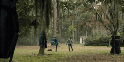 A Man In A Blue Jacket Stands In The Middle Of A Grassy Field In The Woods GIF