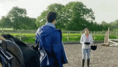 A Man In A Blue Jacket Stands Next To A Woman Holding A Helmet GIF