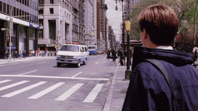 A Man In A Blue Jacket Stands On The Sidewalk Looking At A Crosswalk GIF