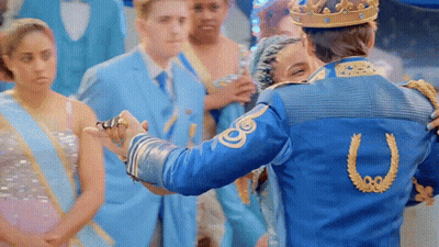 A Man In A Blue Jacket With A Horseshoe On The Back Is Holding A Woman 'S Hand GIF