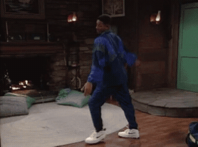 A Man In A Blue Jumpsuit And White Nike Shoes Is Dancing In A Living Room GIF