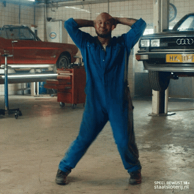 A Man In A Blue Jumpsuit Is Dancing In Front Of An Audi Car GIF