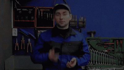 A Man In A Blue Jumpsuit Is Standing In Front Of A Toolbox Filled With Tools . GIF