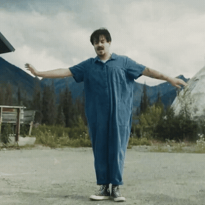 A Man In A Blue Jumpsuit Is Standing With His Arms Outstretched . GIF