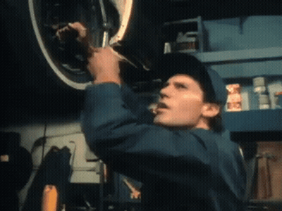 A Man In A Blue Jumpsuit Is Working On A Car GIF