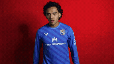 A Man In A Blue Kaiser Permanente Jersey Holds Up A Book GIF