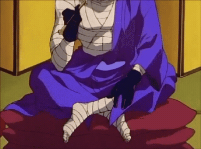 A Man In A Blue Kimono Is Sitting On A Red Pillow With Bandaged Legs . GIF