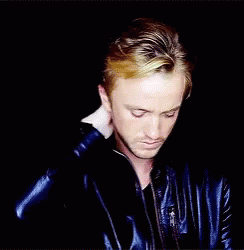 A Man In A Blue Leather Jacket Holds His Hand To His Head GIF