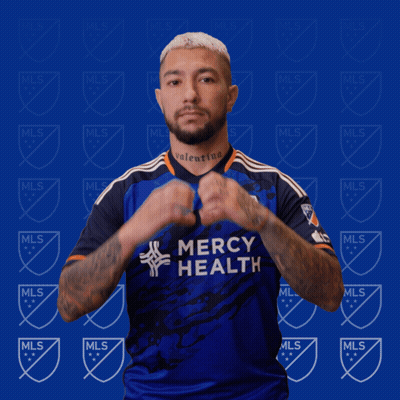 A Man In A Blue Mercy Health Jersey Makes A Heart Shape With His Hands GIF