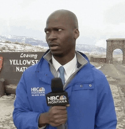 A Man In A Blue Nbc Montana Jacket Holds A Microphone In Front Of A Sign That Says Leaving Yellowstone National Park GIF
