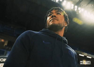 A Man In A Blue Nike Hoodie Stands In A Dark Room With Chelsea Written On The Bottom GIF