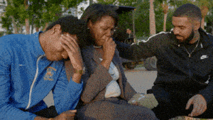 A Man In A Blue Nike Jacket Is Comforting Another Man And Woman GIF