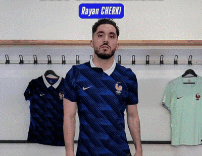 A Man In A Blue Nike Shirt Is Standing In Front Of A Sign That Says Rayan Cherki GIF