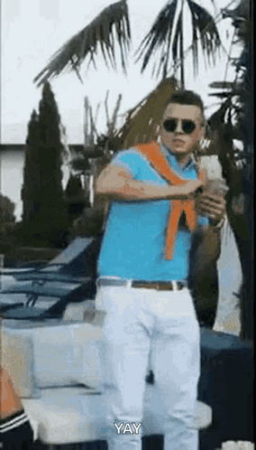 A Man In A Blue Polo Shirt And White Pants Is Standing In Front Of A Palm Tree . GIF