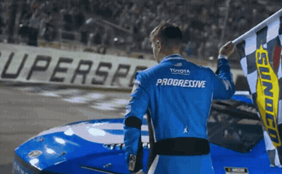 A Man In A Blue Progressive Shirt Holds A Checkered Flag GIF