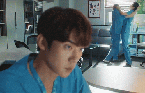 A Man In A Blue Scrub Is Looking At Another Man In A Blue Scrub In A Living Room GIF