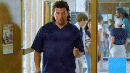 A Man In A Blue Scrub Top Is Standing In A Hallway With People Behind Him . GIF