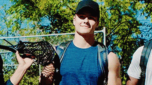 A Man In A Blue Shirt And Black Hat Is Holding A Lacrosse Stick In His Hand . GIF