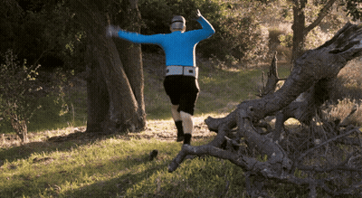 A Man In A Blue Shirt And Black Shorts Is Running Through A Forest GIF