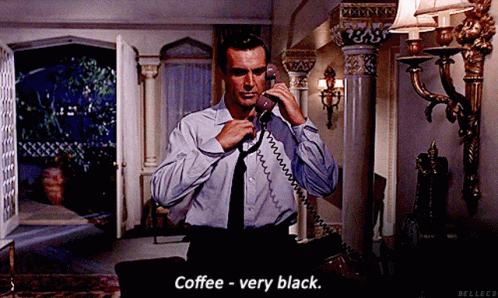 A Man In A Blue Shirt And Black Tie Is Talking On A Phone And Says Coffee - Very Black GIF
