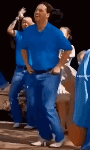 A Man In A Blue Shirt And Blue Jeans Is Dancing In A Crowd . GIF
