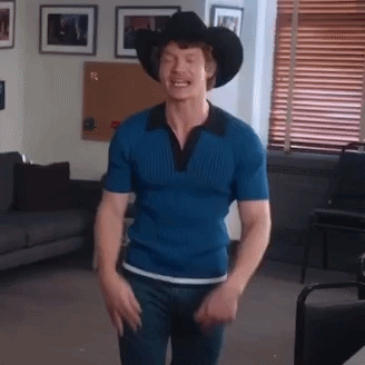 A Man In A Blue Shirt And Cowboy Hat Is Dancing In A Living Room . GIF