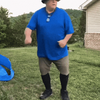 A Man In A Blue Shirt And Hat Is Dancing In A Yard GIF