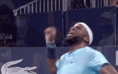 A Man In A Blue Shirt And Headband Is Standing On A Tennis Court With His Arms Outstretched . GIF