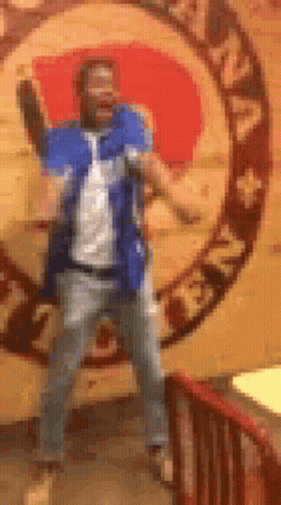 A Man In A Blue Shirt And Jeans Is Dancing In Front Of A Wall With A Zodiac Sign . GIF