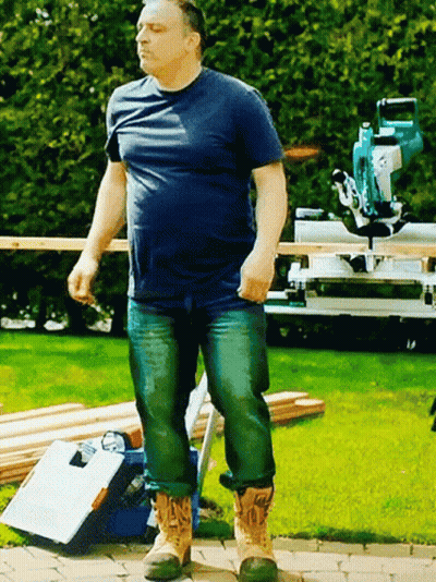 A Man In A Blue Shirt And Jeans Is Standing On A Sidewalk GIF