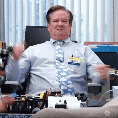 A Man In A Blue Shirt And Tie Is Sitting At A Desk In An Office Making A Funny Face . GIF