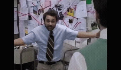 A Man In A Blue Shirt And Tie Is Standing In Front Of A Bulletin Board With Papers On It . GIF