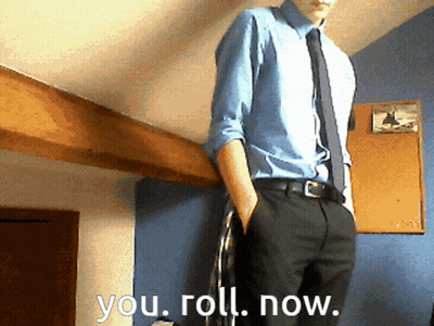 A Man In A Blue Shirt And Tie Is Standing In Front Of A Wall That Says You Roll Now GIF