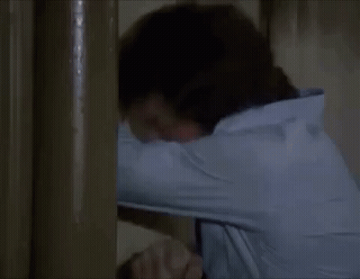 A Man In A Blue Shirt And Tie Is Standing Next To A Wall . GIF