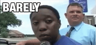 A Man In A Blue Shirt And Tie Is Talking Into A Microphone In Front Of A Man In A Suit . GIF