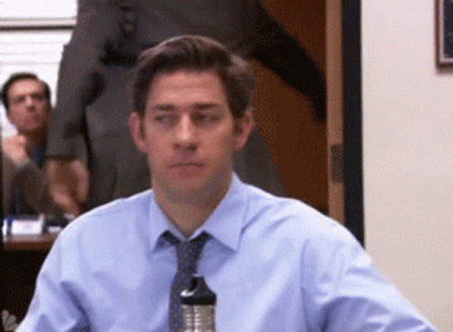A Man In A Blue Shirt And Tie Sits At A Table GIF
