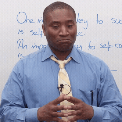 A Man In A Blue Shirt And Tie Stands In Front Of A White Board With The Words One In Key To Self Written On It GIF