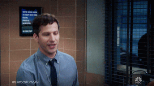 A Man In A Blue Shirt And Tie Stands In Front Of A Window With A Sign That Says Brooklyn99 GIF