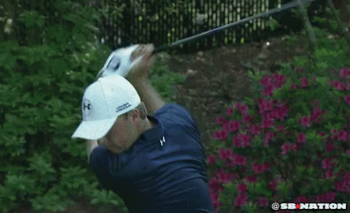 A Man In A Blue Shirt And White Hat Is Swinging A Golf Club . GIF