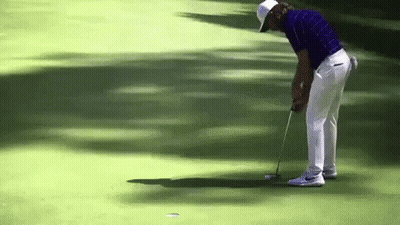 A Man In A Blue Shirt And White Pants Is Putting A Golf Ball GIF