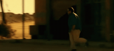 A Man In A Blue Shirt And White Pants Is Walking Down A Street . GIF