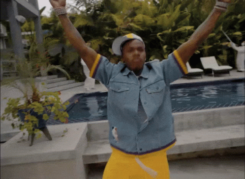 A Man In A Blue Shirt And Yellow Shorts Is Standing In Front Of A Swimming Pool GIF