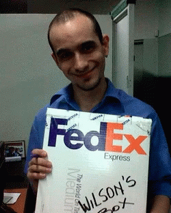 A Man In A Blue Shirt Holds Up A Fedex Express Box GIF