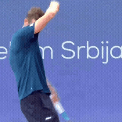 A Man In A Blue Shirt Is Bending Over In Front Of A Sign That Says Elek S. GIF