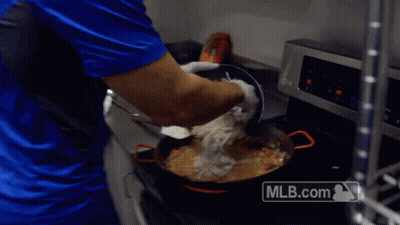 A Man In A Blue Shirt Is Cooking In A Kitchen With A Mlb.com Logo On The Stove GIF