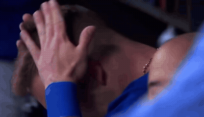 A Man In A Blue Shirt Is Covering His Face With His Hands While A Woman Holds His Head . GIF