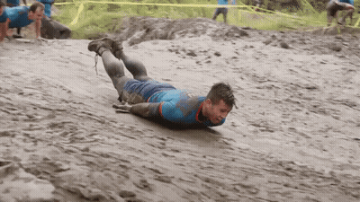 A Man In A Blue Shirt Is Crawling In The Mud . GIF