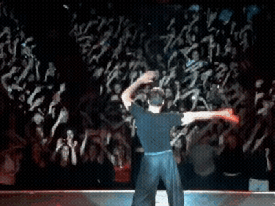 A Man In A Blue Shirt Is Dancing In Front Of A Crowd Of People . GIF